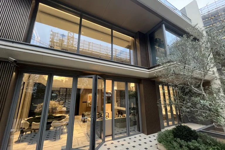 High-end private villa in Medan Indonesia at dusk, with a six-panel thermal-break aluminium folding glass door system opening from the principal living room to a stone-tiled patio and a planted olive tree