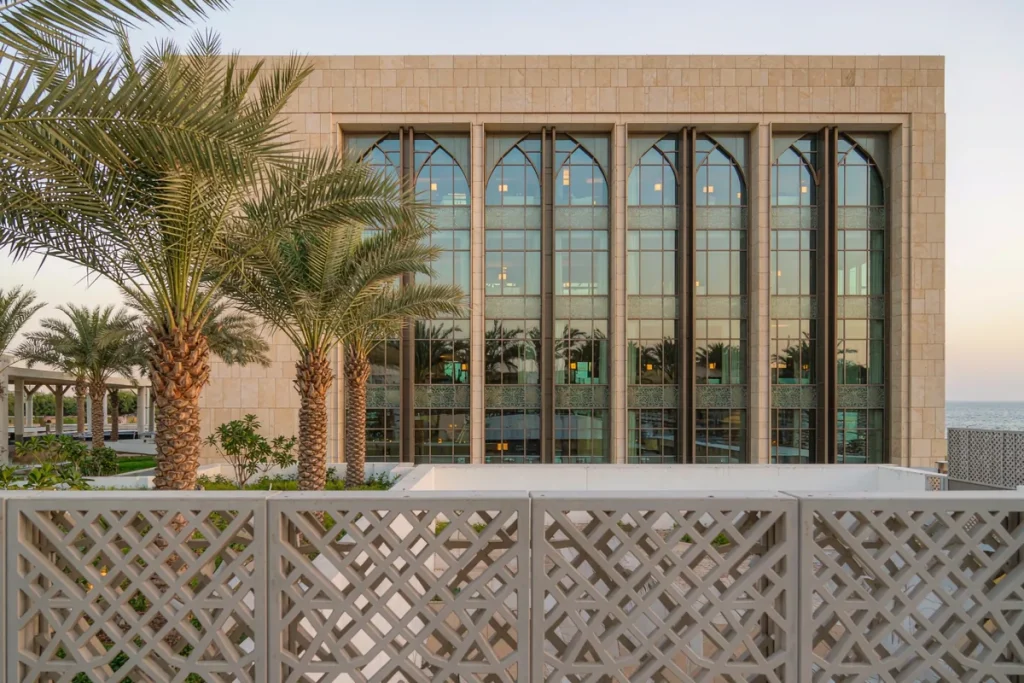 Coastal villa in Dubai with a CNC-patterned aluminium mashrabiya shading screen over a glazed curtain wall courtyard elevation