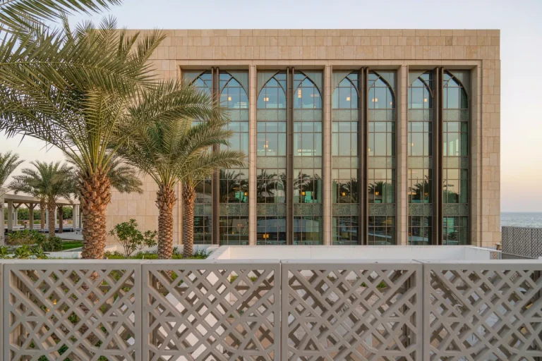 Coastal villa in Dubai with a CNC-patterned aluminium mashrabiya shading screen over a glazed curtain wall courtyard elevation